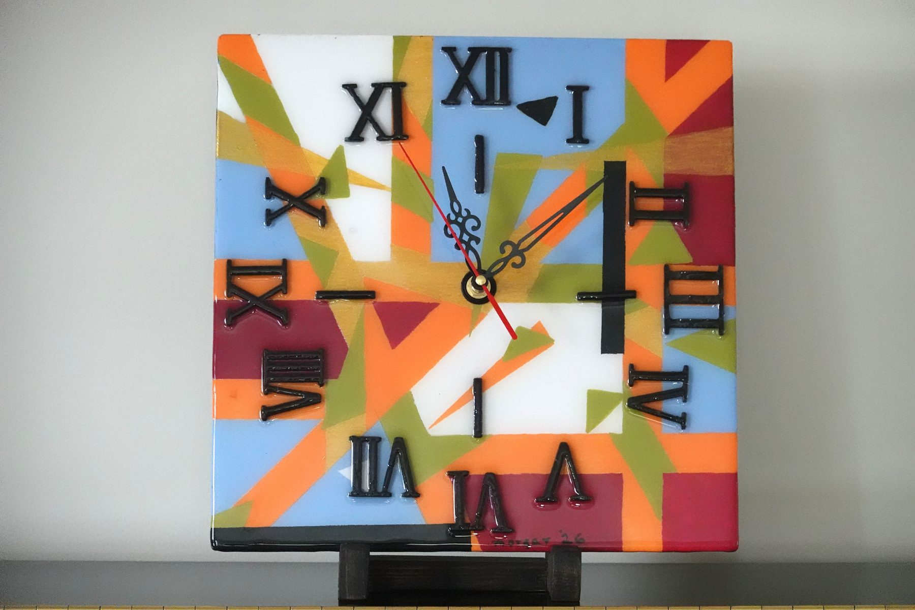 Sunray Fracture clock, a square abstract painted resin clock with radiating orange, blue and olive geometric rays
