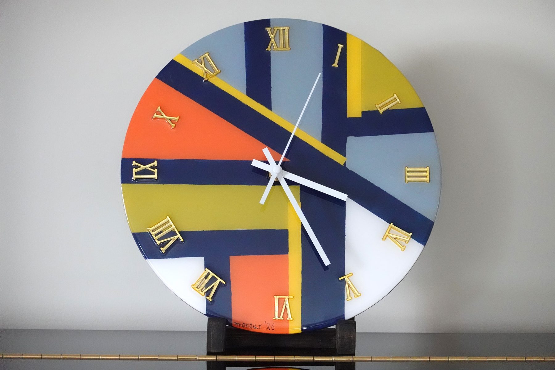 Diagonal Fields clock, a circular abstract painted resin clock with diagonal navy and yellow bands over orange, blue and white blocks