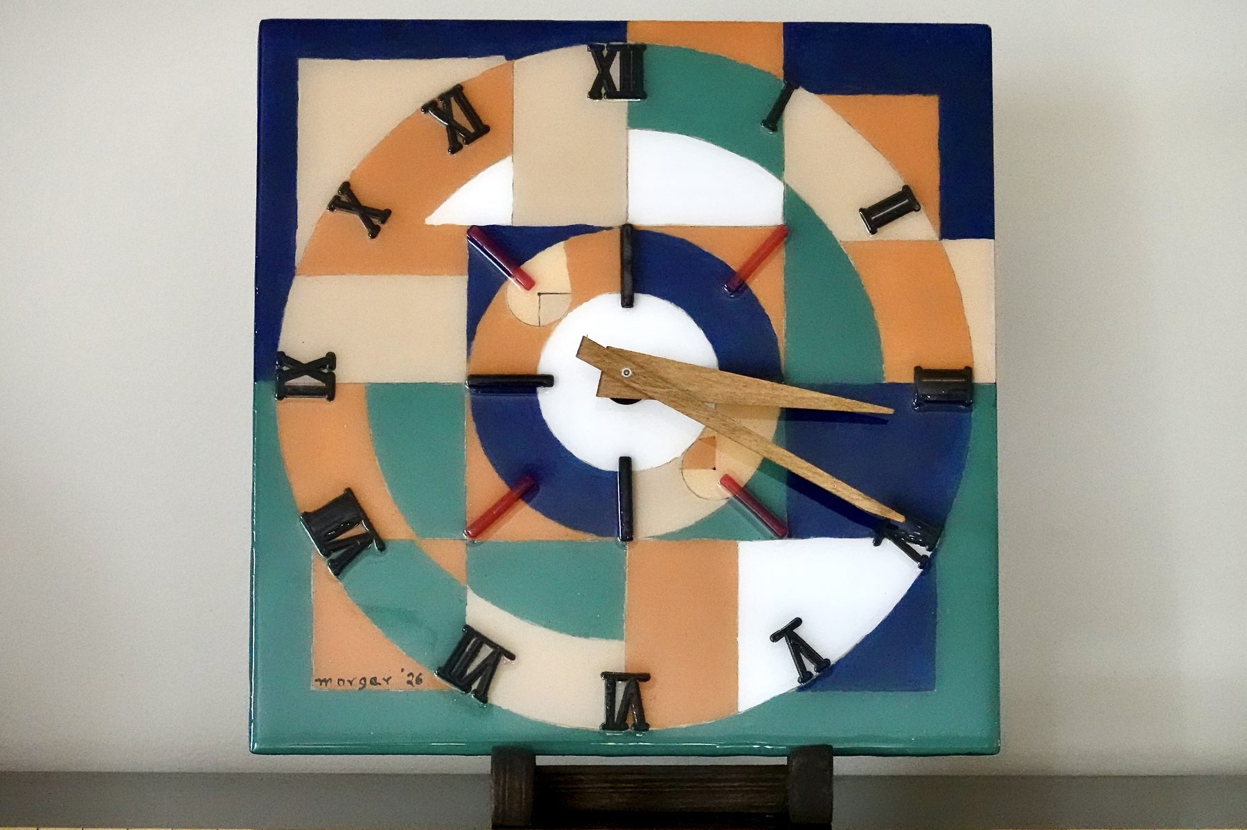 Radial Fields clock, a square abstract painted resin clock with concentric ring and grid patterns in navy, teal, tan and orange